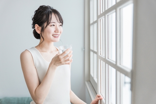 明るい窓辺で水を飲む女性